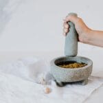 Dłoń ucierająca świeże pesto w kamiennym moździerzu