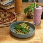 Makaron z pesto genovese obok pizzy i koktajli na drewnianym stole