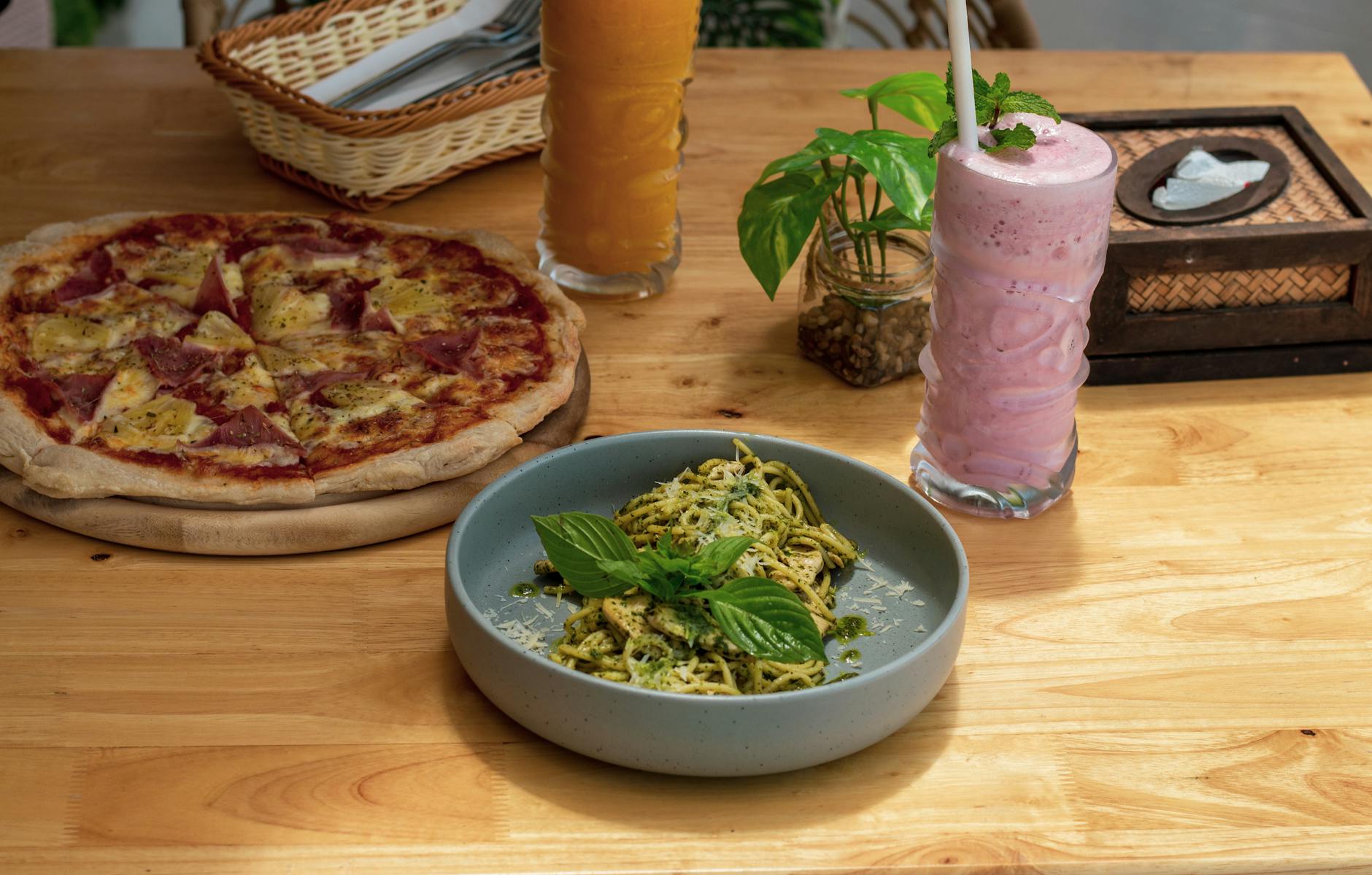 Makaron z pesto genovese obok pizzy i koktajli na drewnianym stole
