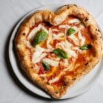 Pizza margherita w kształcie serca z mozzarellą i bazylią na białym talerzu