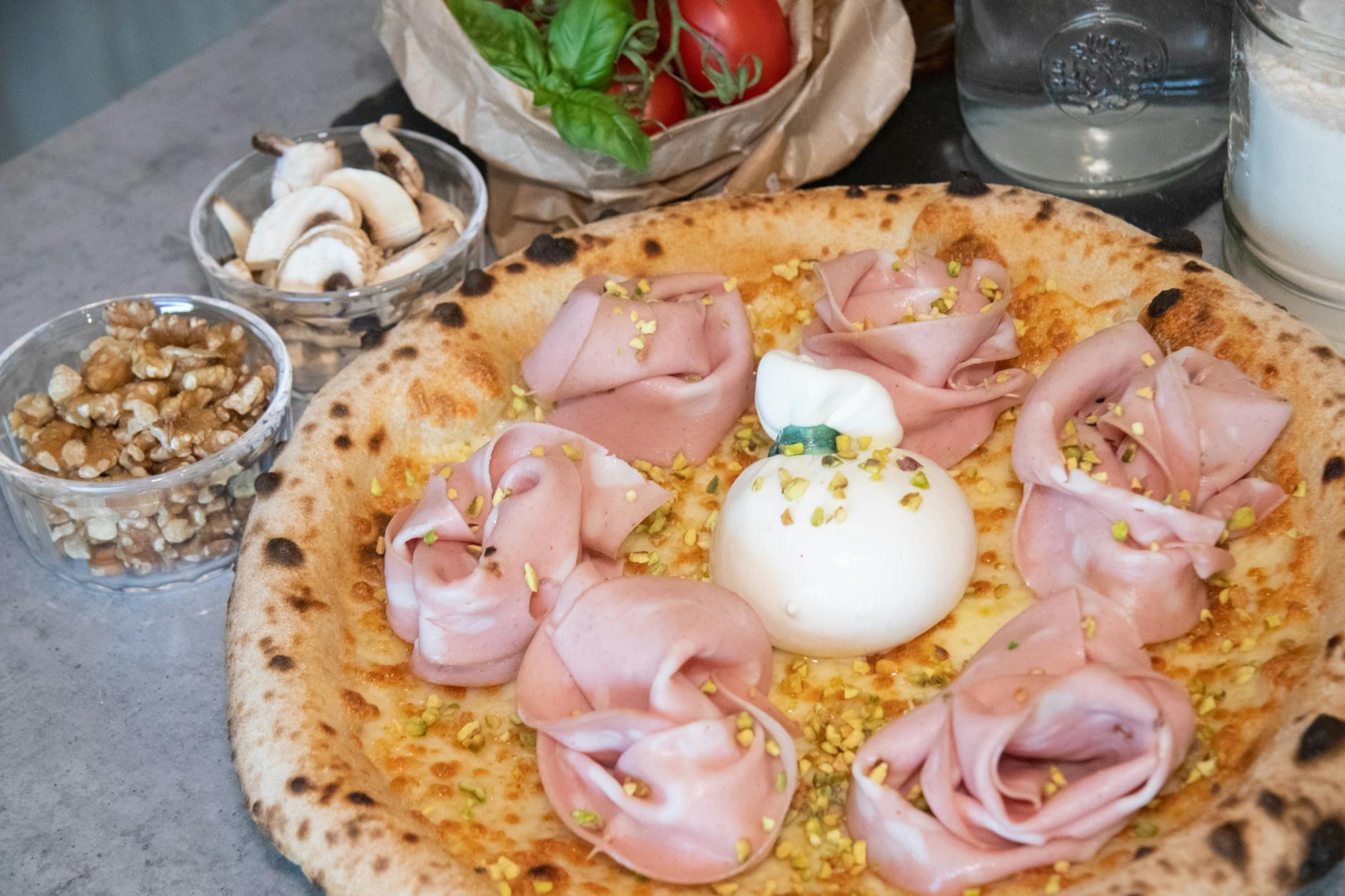 Pizza z mortadelą, burratą i posypką z pistacji na drewnianej desce Pizza z mortadelą, burratą i posypką z pistacji na drewnianej desce