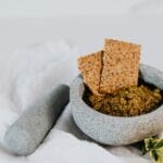 Moździerz z pesto genovese i chrupkie pieczywo na białym obrusie