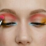 Zbliżenie oka z pędzelkiem nakładającym różowy, niebieski i żółty cień