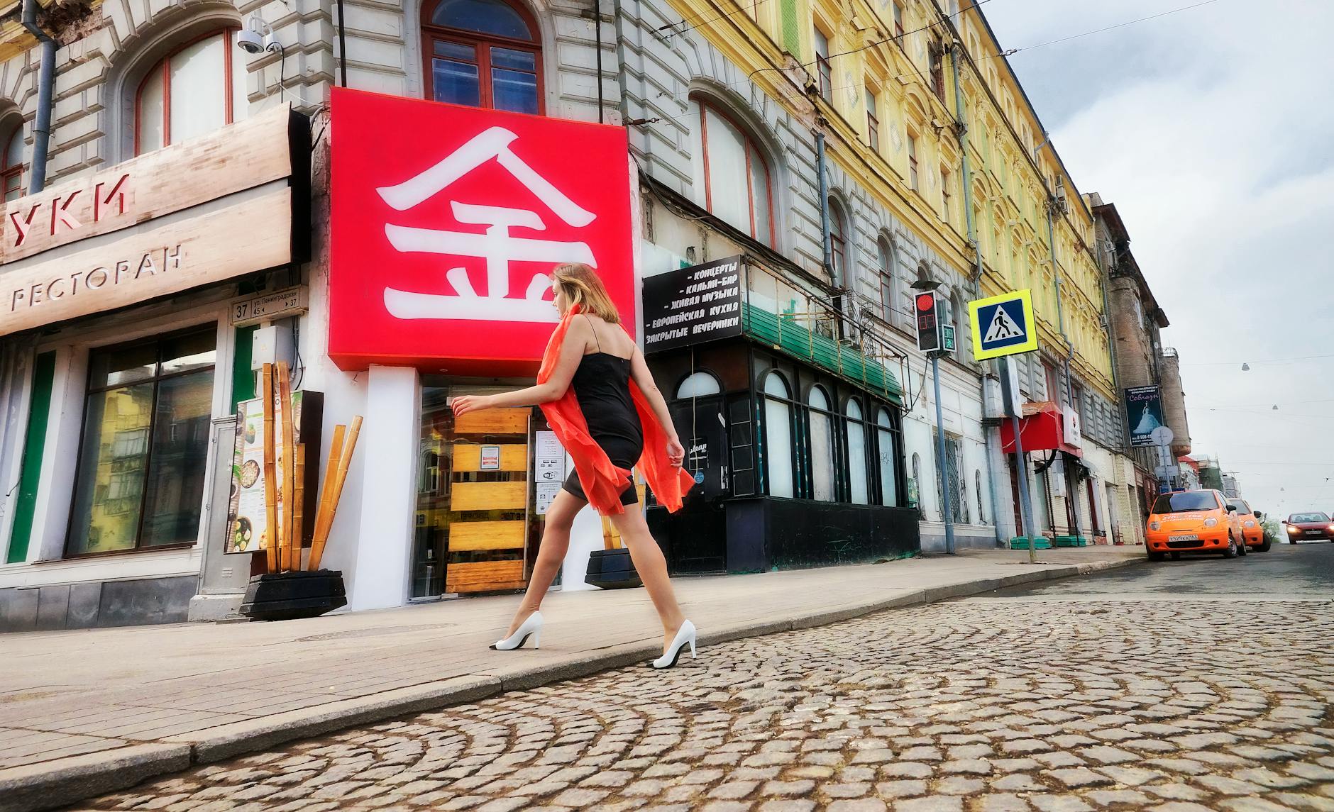 Kobieta w czarnej sukience z czerwonym szalem idzie przez miasto