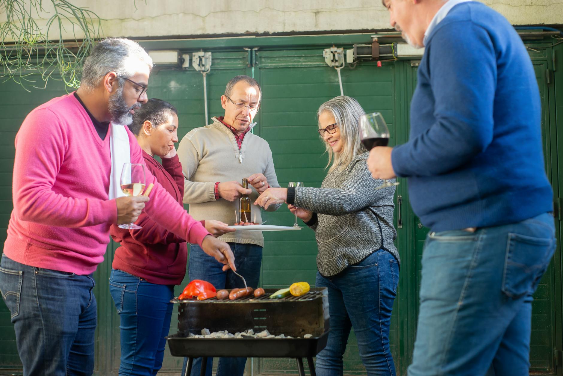 Przyjaciele przy grillu w ogrodzie, piją wino do potraw z rusztu