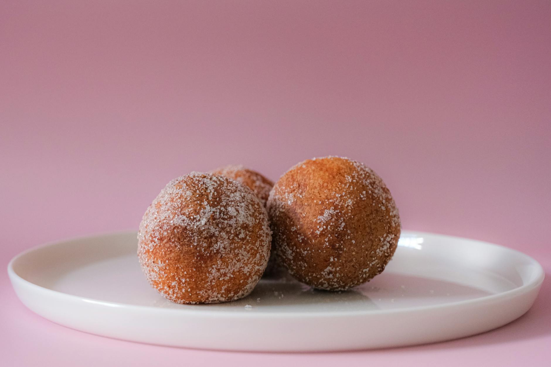 Włoskie kulki struffoli w cukrze na białym talerzu na różowym tle