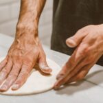 Jak zrobić pizzę na zakwasie: smak, struktura i prowadzenie ciasta bez stresu Dłonie formujące ciasto na pizzę na zakwasie z bliska