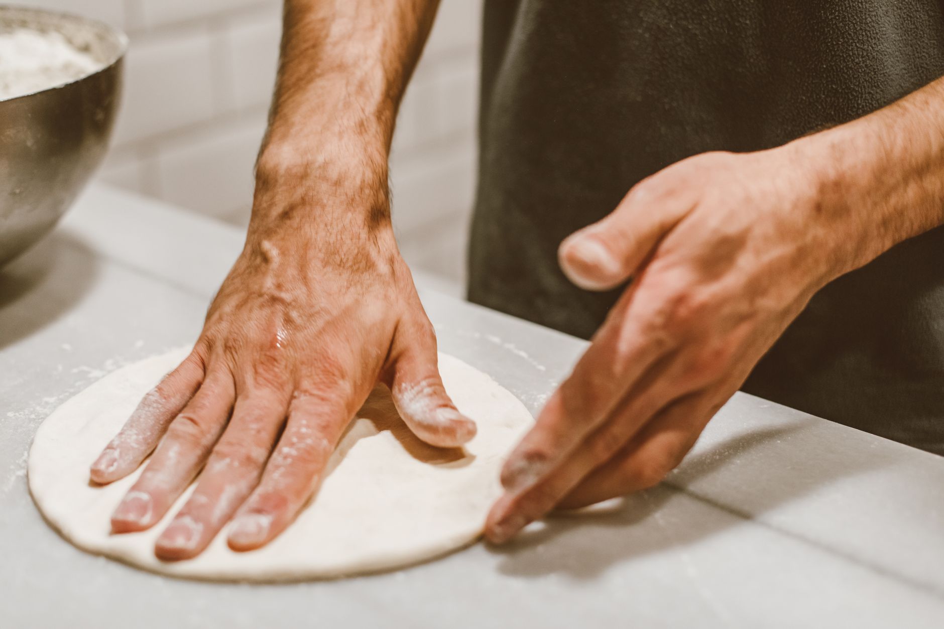 Jak zrobić pizzę na zakwasie: smak, struktura i prowadzenie ciasta bez stresu Dłonie formujące ciasto na pizzę na zakwasie z bliska