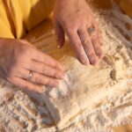 Dłonie zagniatają ciasto na pizzę na oprószonym mąką blacie