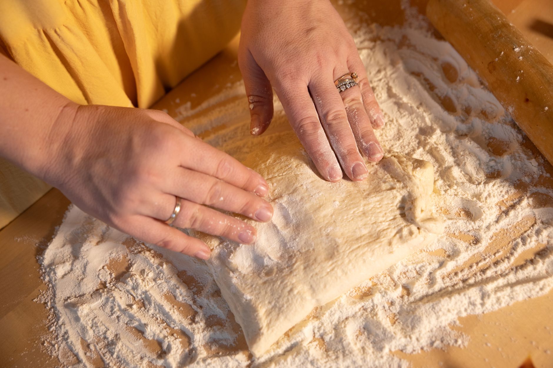 Dłonie zagniatają ciasto na pizzę na oprószonym mąką blacie