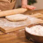 Ręce wałkują ciasto na pizzę na oprószonej mąką drewnianej desce
