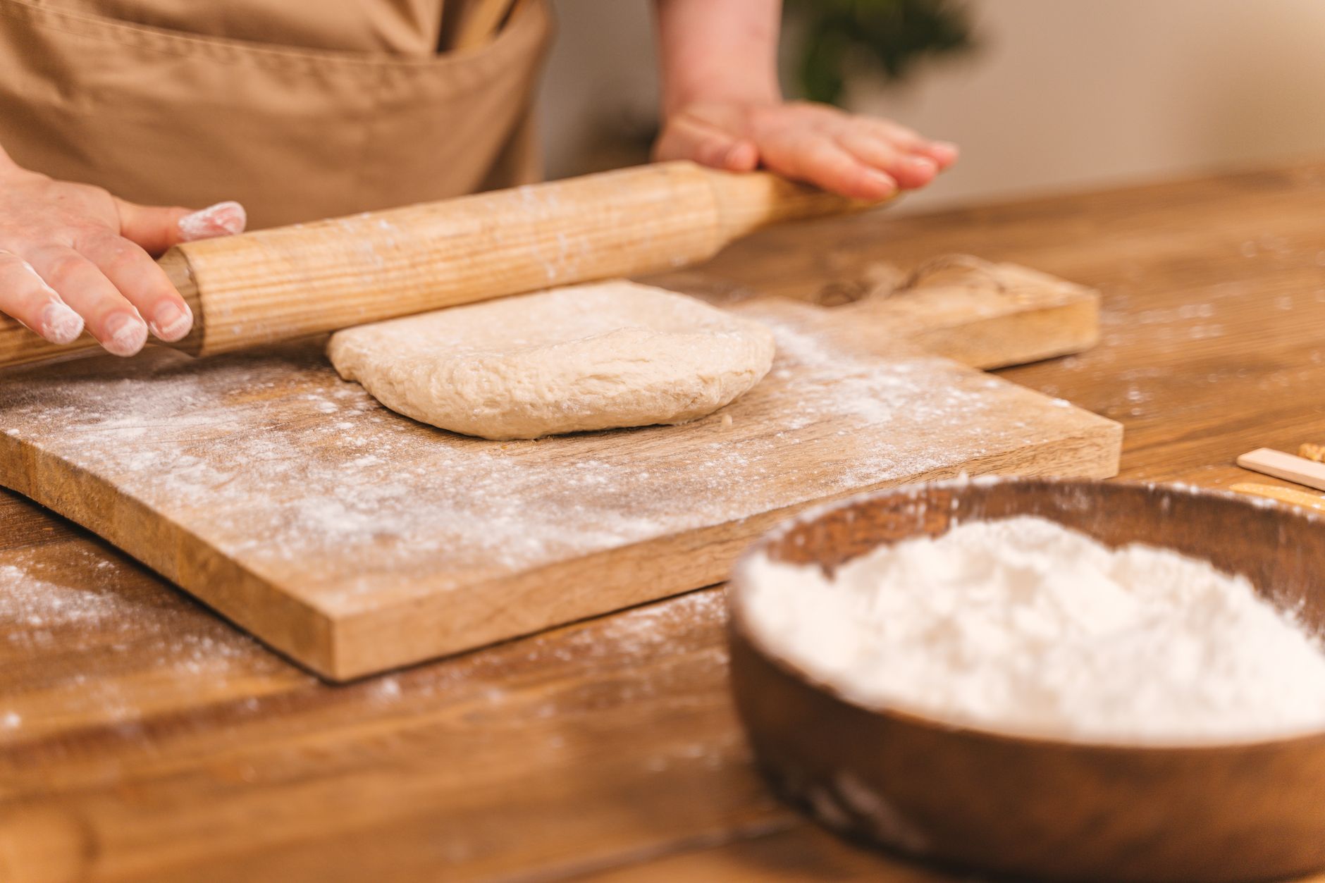 Ręce wałkują ciasto na pizzę na oprószonej mąką drewnianej desce