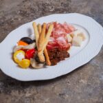 Włoskie antipasti z grissini, wędlinami i serami na białym talerzu